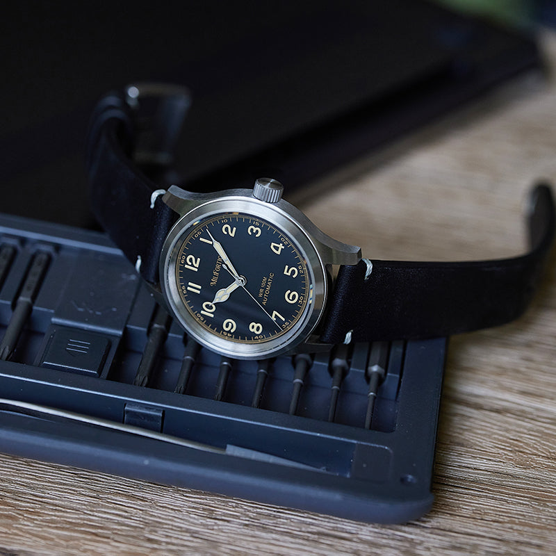 Black military watch lying sideways on a screw tool