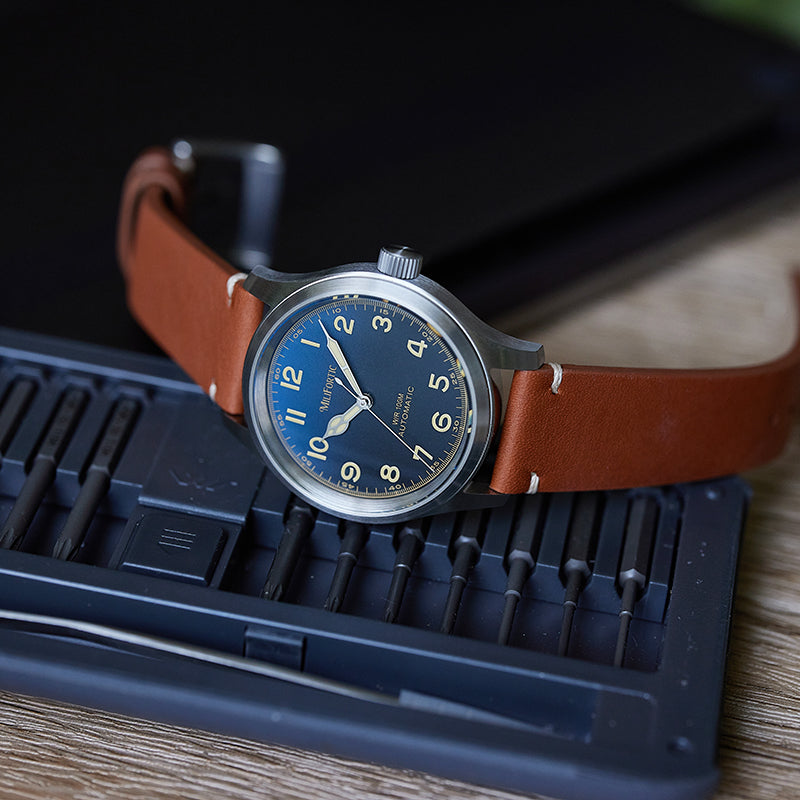 Blue dial automatic watch with brown strap, placed sideways on a screw toolbox