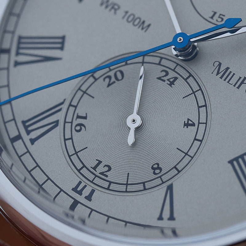 Gray dial close-up featuring a 24-hour subdial, heat-blued hands