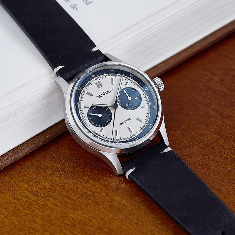 R078 American classic homage watch with black dial, black leather strap, angled on the side of a book.