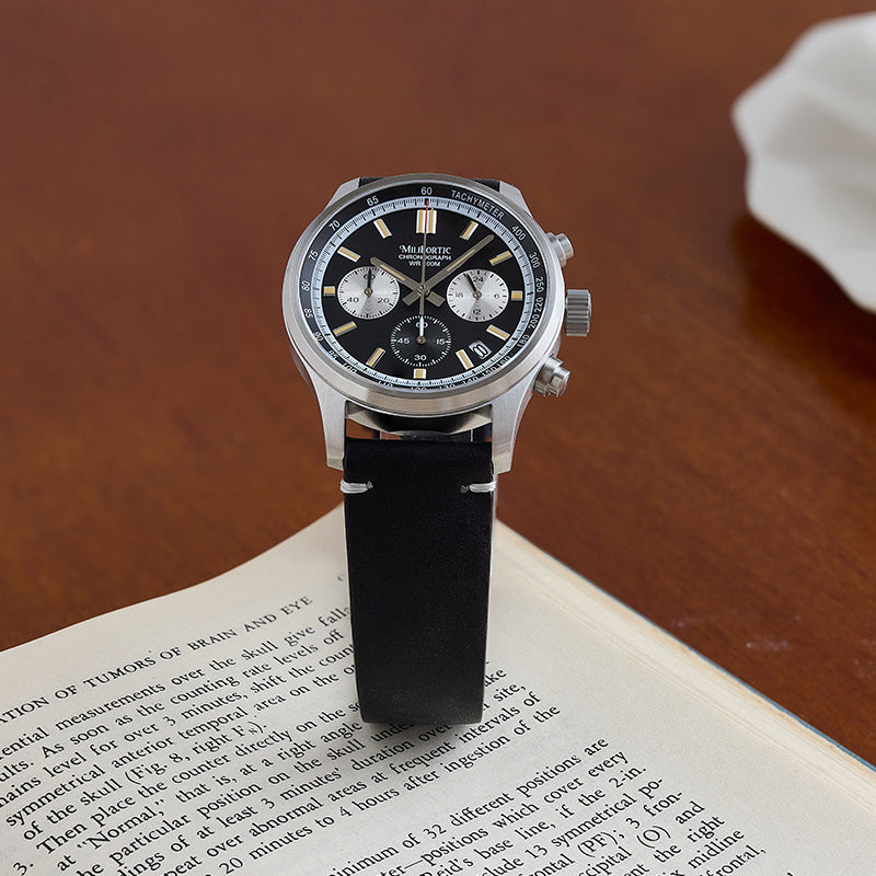 Black chronograph watch standing on top of an English book